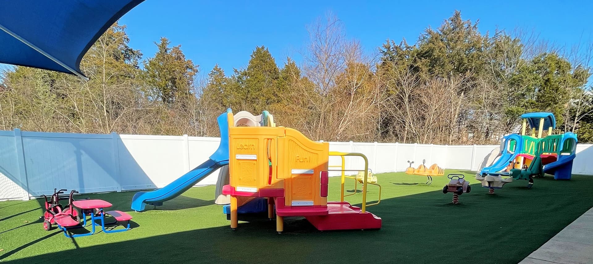 The fenced Sterling playground with slides, climbing structures and ride-on toys on green turf
