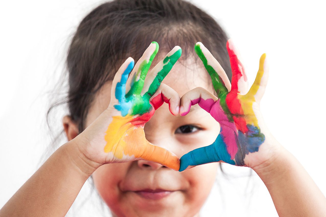 Preschool child making heart with painted hands.