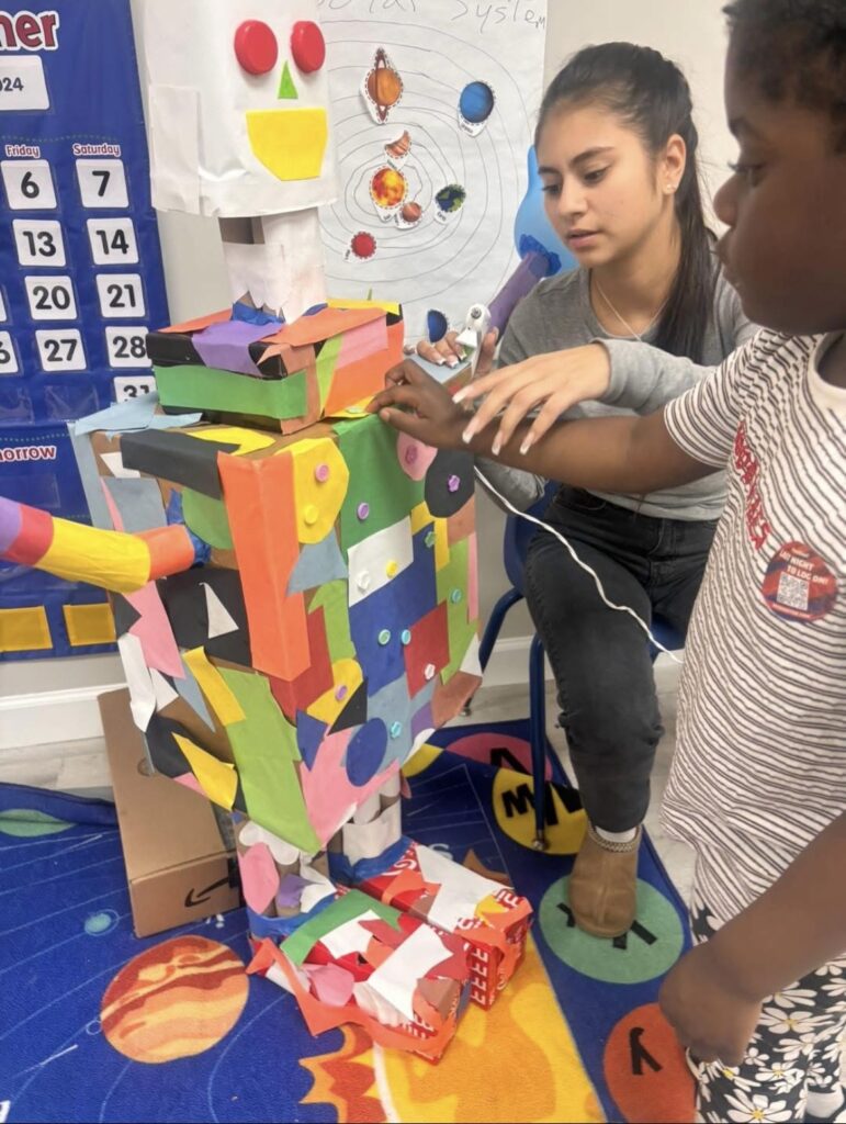 Students add pieces of colored paper to a robot made of cardboard.